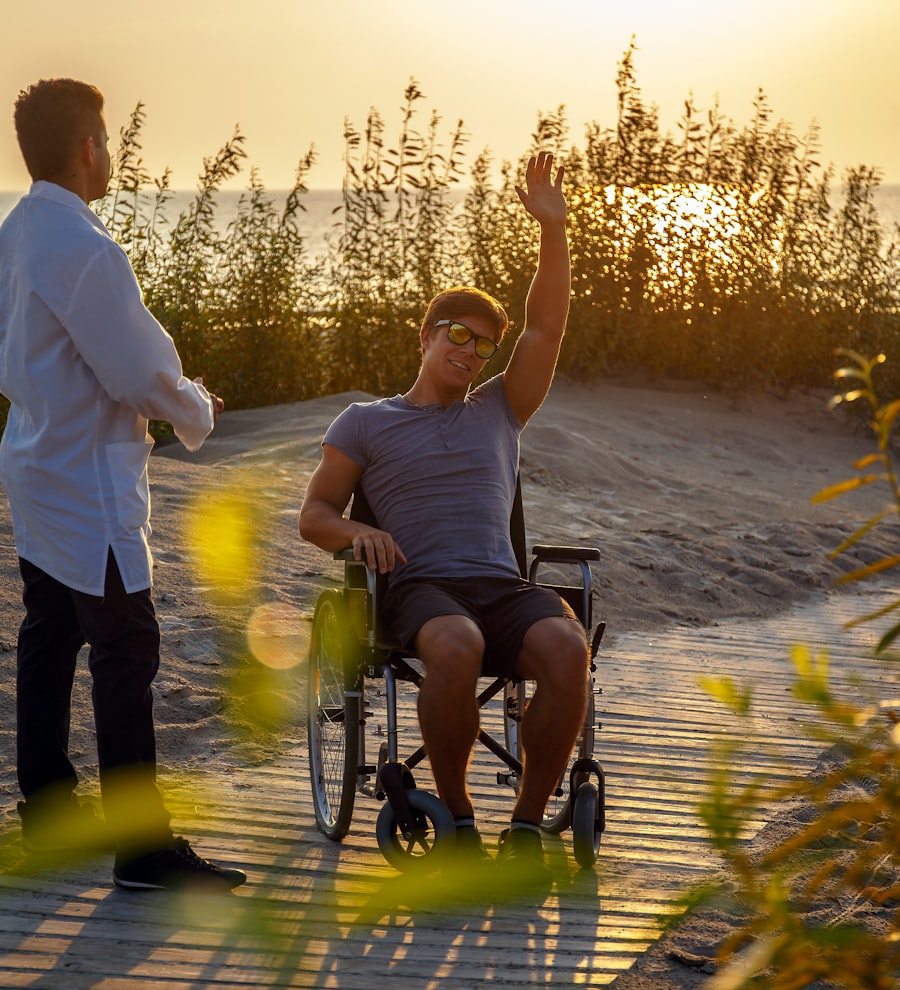 A young man in a wheelchair waving happily on a beach boardwalk at sunset